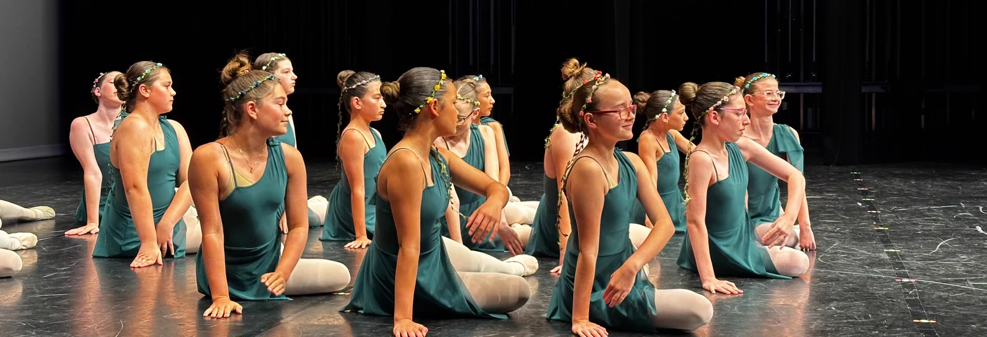 Serendipity dancers seated together on stage in teal costumes